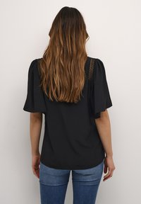 Blusa nera con maniche a sbuffo corte, caratterizzata da un dettaglio in pizzo sulle spalle. Indossata con jeans di denim blu, vista da dietro.