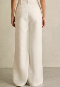 Brede broek in een romige witte stof. Beschikt over twee achterzakken en een glad, strak ontwerp met een op maat gemaakte taille.