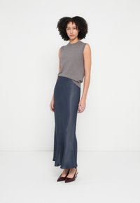 Pelēks bezroku adīts tops, kopā ar tumši zilu satīna maksi svārkiem. Svārkiem ir plūstošs dizains un viegla spīduma. Burgundijas krāsas kurpes ar smailiem purngaliem.