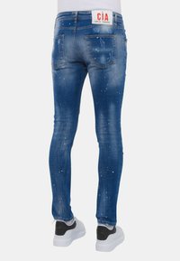 Blauwe denim jeans met een slim fit, voorzien van een licht afgesleten ontwerp en details van witte verfspatten. Achterlabel gemarkeerd met "CIA LOCAL FANATIC."