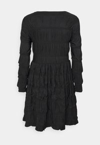 Robe noire à manches longues avec une texture froncée, taille ajustée et jupe légèrement évasée, vue de dos sur un fond uni.