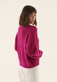 Pull en tricot magenta à coupe décontractée, manches larges et texture côtelée. Présente un large col et un design en couleur unie.