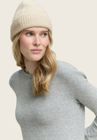 Berretto lavorato a maglia color beige chiaro con texture a coste, abbinato a un maglione fitted in lana grigia. Tessuto morbido e liscio con scollatura a girocollo classica.