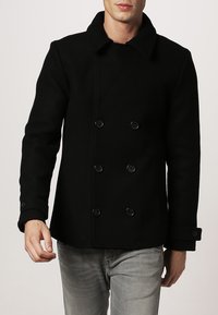 Cappotto nero doppiopetto con grandi bottoni, colletto a rever e maniche lunghe. Realizzato in un tessuto strutturato, offre un aspetto definito.