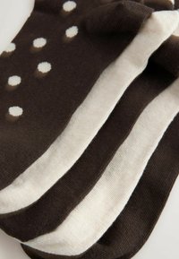 Rudos ir kremiškai baltos kojinės su dryžuotu raštu, kurioje pakaitomis yra baltos taškuotos sekcijos. Minkšta tekstūra ir smulkiai megztas audinys.