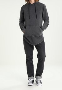 Tmavě šedá mikina s klokaní kapsou, žebrovanými rukávy a nastavitelnými šňůrkami, kombinovaná s černými úzkými džíny a černými teniskami.