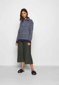 Navy patterned pullover with a quarter zip, paired with gray wide-leg pants and dark slippers. Emphasizes cozy, casual wear.
