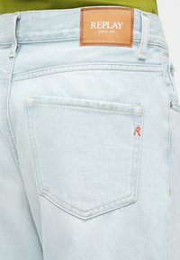 Φωτεινά μπλε τζιν από τζιν ύφασμα με δερμάτινη ετικέτα στη μέση που γράφει "REPLAY SINCE 1981" και κεντημένο κόκκινο "R" στην πίσω τσέπη.