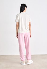 Lichtgrijs T-shirt met korte mouwen, gecombineerd met een roze trainingsbroek met elastische boorden, gedragen met witte sneakers. Eenvoudige, casual outfit.