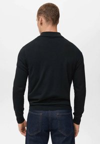 Schwarzes Langarm-Polohemd mit geripptem Kragen, taillierten Manschetten und glatter Textur, kombiniert mit dunklen Jeans.