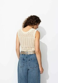 Top crème en tricot avec un motif en dentelle complexe et un col festonné, associé à un jean en denim bleu taille haute et une ceinture en métal tressée.