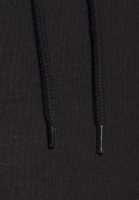Tissu de sweat à capuche noir avec gros plan sur deux cordons tressés se terminant par des embouts en plastique noir.