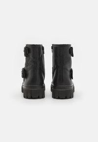 Las botas negras de cuero hasta el tobillo presentan un acabado texturizado, una suela de plataforma gruesa y cremalleras laterales con hebillas decorativas en el exterior.
