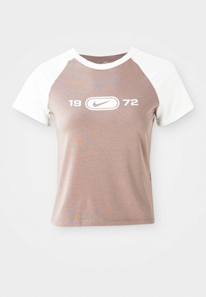 T-shirt κοντής μανικιού με σώμα ανοιχτού καφέ και λευκά ράγλαν μανίκια, που διαθέτει ένα μεγάλο λευκό γραφικό λογότυπο και το έτος "1972" κεντραρισμένο στο μπροστινό μέρος.