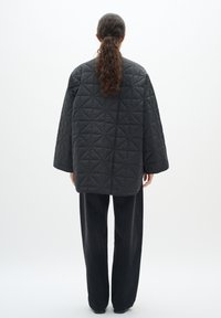 Giacca nera oversized trapuntata realizzata in materiale sintetico con un motivo geometrico, abbinata a pantaloni neri a gamba dritta.
