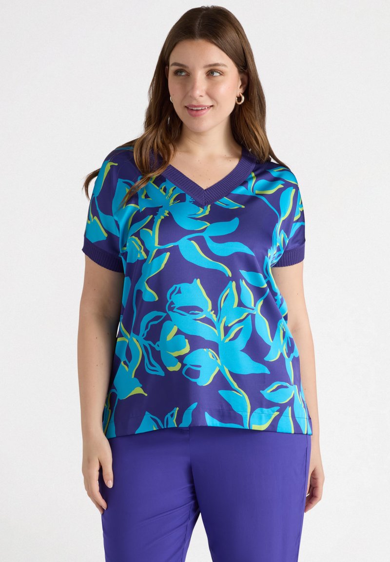 T-shirt à manches courtes en bleu marine avec un motif floral teal vif. Doté d'un col en V et de finitions côtelées. Associé à un pantalon violet uni.