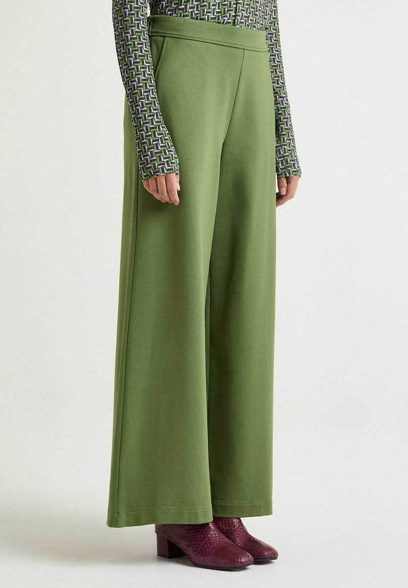 Pantaloni verde a gamba larga realizzati in tessuto morbido, con un design pulito e vita alta. Abbinati a stivaletti bordeaux con texture.