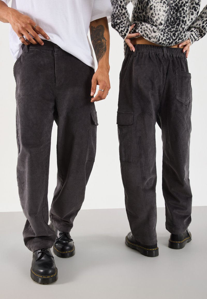 Gray corduroy pants featuring a relaxed fit, elastic waistband, and side pockets. Paired with black shoes, showcasing a textured fabric.