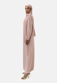 Abito lungo e fluente in morbido tessuto rosa, con maniche lunghe, polsini a palloncino e un hijab coordinato. Colore uniforme con elementi di design minimali.