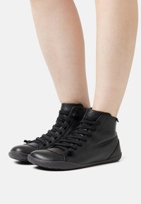 Stivaletti neri in pelle con punta tondeggiante, caratterizzati da un design con lacci, superficie testurizzata e uno stile minimalista.