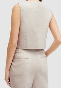 Ljust beige urklippt topp med en slät, linnetextur och en subtil lyster. Har en rund halsringning och en ren, minimalistisk baksidedesign.