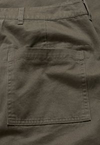 Tmavě zelené bavlněné šortky s kapsou na zadní straně, která má obdélníkový tvar, ploché švy a hladkou texturu. Minimalistické designové prvky.