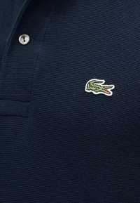 Polo bleu marine en tissu texturé, avec un petit logo crocodile vert brodé sur la poitrine gauche et un bouton près du col.