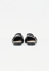 Sandales en cuir noir avec dos ouvert, dotées de brides texturées et d'une semelle plate. Design simple avec une esthétique minimaliste.