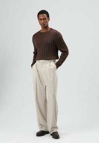 Bruine geribbelde gebreide trui met lange mouwen, gecombineerd met roomkleurige hoge taille plissébroek en donkerbruine schoenen.