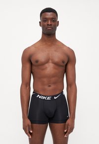Boxeri negri Nike cu un brâu alb în contrast, având logo-ul Nike. Materialul pare neted și se mulează pe corp.