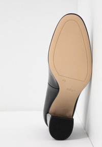 Czarny skórzany but na obcasie z gładkim wykończeniem, z okrągłym noskiem, beżową podeszwą oraz subtelnym logo na obcasie.