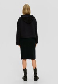 Zwarte cropped hoodie met een capuchon, gecombineerd met een donkere gebreide rok en zwarte chunky laarzen. Soepele textuur en een ontspannen pasvorm zijn zichtbaar.