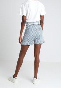 Wysokiej talii szorty w niebiesko-białe paski z bawełny, z przodem zapinanym na guziki, szlufkami na pasek i bocznymi kieszeniami, zestawione z białą koszulą i trampkami.