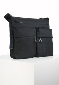 Schwarze Umhängetasche mit zwei vorderen Reißverschlusstaschen, strukturiertem Stoff, verstellbarem Tragegurt und eingeprägtem Logodesign. Minimalistisches Design und robuste Hardware.