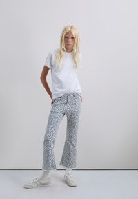 Tricou alb cu mânecă scurtă, blugi scurți cu un model bleu deschis și accente roșii și bleumarin, și pantofi sport crem cu șosete albe.