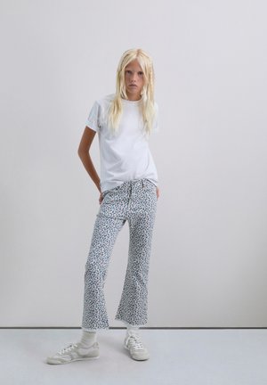 Camiseta blanca de manga corta, jeans cortos de color azul claro con estampado y acentos rojos y marinos, y zapatillas color crema con calcetines blancos.