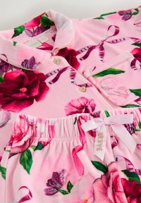 Floral Pyjama-Set aus pinkem Plüschmaterial. Mit großen Rosenprints, herzförmigen Knöpfen und einem Bindeband am elastischen Taillengummi.