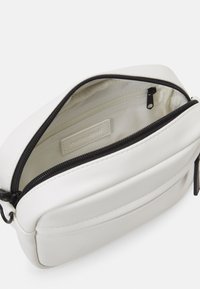 Pochette sintetica bianca con chiusura a zip. L'interno presenta una fodera in tessuto leggero e una tasca piccola. L'esterno ha una forma liscia e arrotondata.