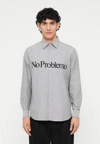 Harmaa nappikauluspaita pitkillä hihoilla, jossa on musta "No Problemo" -grafiikka rinnassa ja klassinen kaulus.