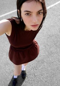 Rochie burgundă cu guler rotund, fustă evazată, mâneci scurte și material texturat. Pantofi negri cu șosete albe, așezați pe un fundal gri.