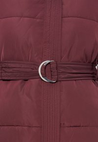Veste matelassée grenat avec ceinture cousue dotée d'une boucle en D argentée brillante à la taille.