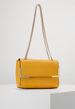 Sac à bandoulière en cuir jaune texturé avec une chaîne dorée et des accents métalliques aux coins, présenté sur un piédestal blanc sur un fond neutre.