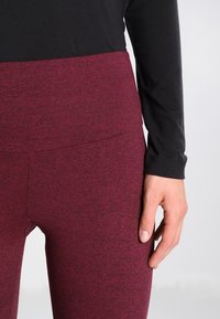Leggings bordeaux a vita alta realizzati in tessuto elasticizzato, con un design semplice e una texture liscia, abbinati a una maglietta nera a maniche lunghe.