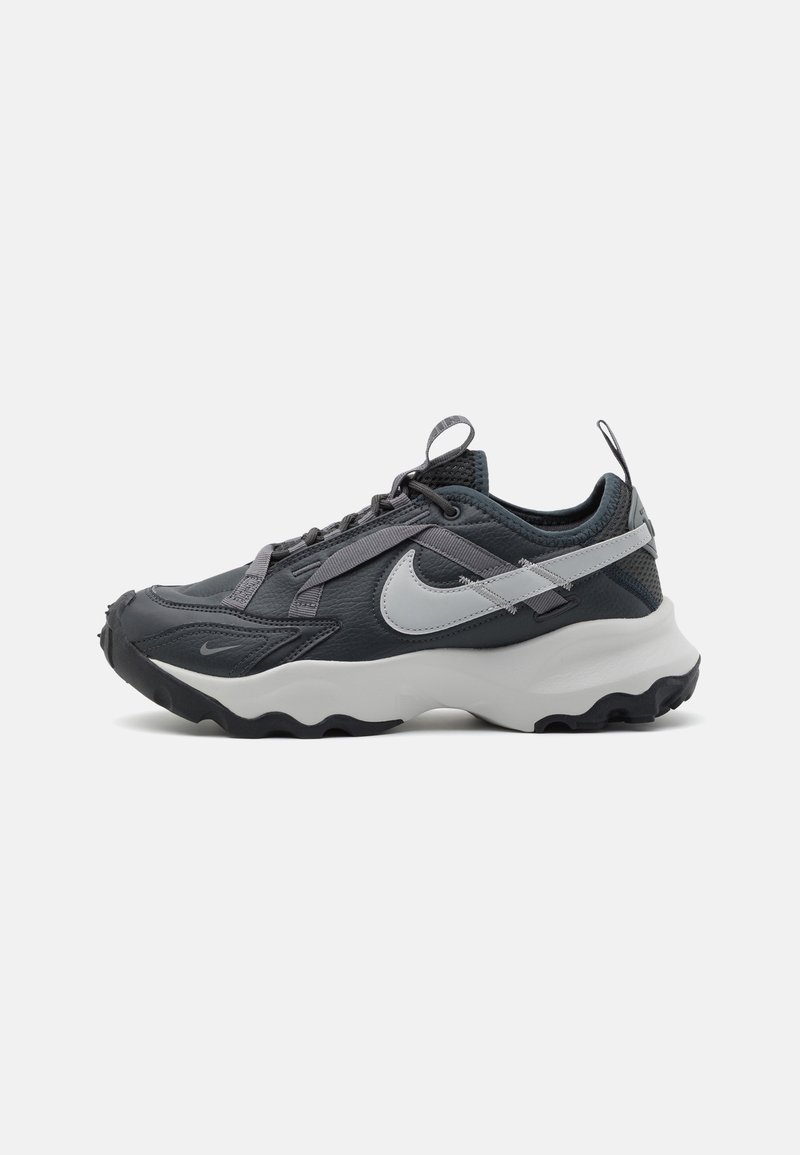 Baskets Nike gris foncé et noir avec une semelle intermédiaire blanche, un grand swoosh blanc, un design en tissu superposé et des languettes sur la languette et le talon.