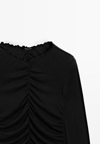 Maglietta nera a maniche lunghe con scollatura a onde e texture arricciata sul davanti. Il tessuto sembra morbido con una finitura liscia.