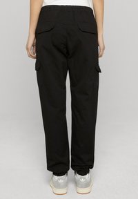 Mustad tööpüksid elastse vöökohaga, kahe tagatasku ja mansetiga sääreotstega, kombineeritud hallide vabaajajalanõudega. Sile kangapind.