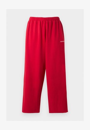 Pantalon de jogging rouge coupe ample avec taille élastique et petit logo blanc sur la cuisse droite, présenté sur fond uni.