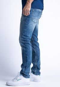 Wyblakłe, niebieskie dżinsy o prostym kroju, z kieszeniami i subtelnymi przetarciami, zestawione z białymi trampkami.