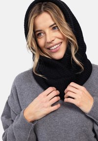 Czarny dzianinowy golf, o miękkiej teksturze, z przytulnym designem. Noszony na szarym oversize'owym swetrze, dogodnie układający się wokół twarzy.