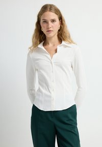 Witte long sleeve overhemd met puntkraag, textuurstof en subtiele placketdetails, gecombineerd met donkergroene broek.